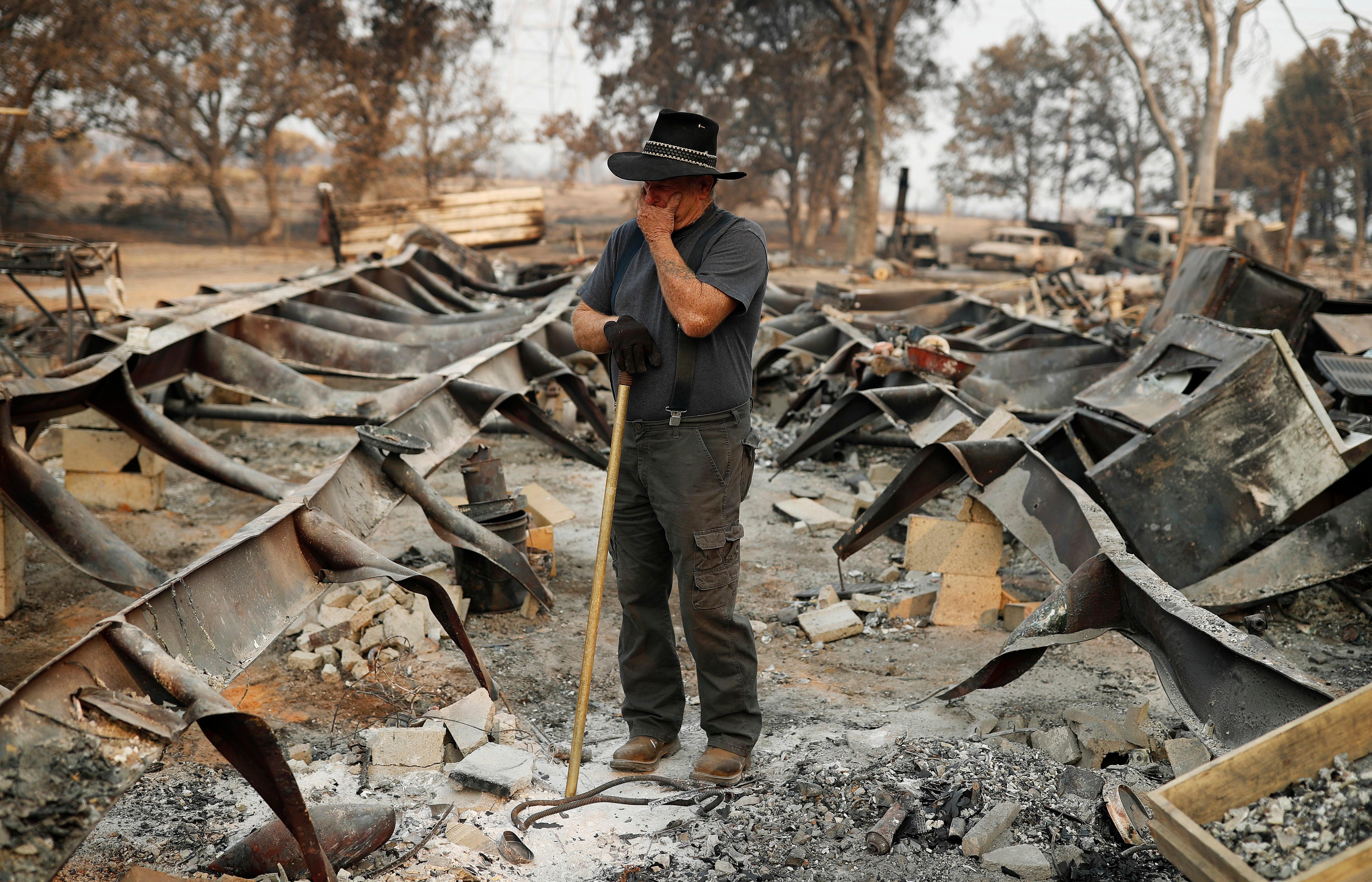Ed Bledsoe tries to hold back tears as he searches through what remains of his home, Aug. 13, 2018, in Redding, Calif. Bledsoe's wife, Melody, great-grandson James Roberts and great-granddaughter Emily Roberts were killed at the home in the Carr Fire