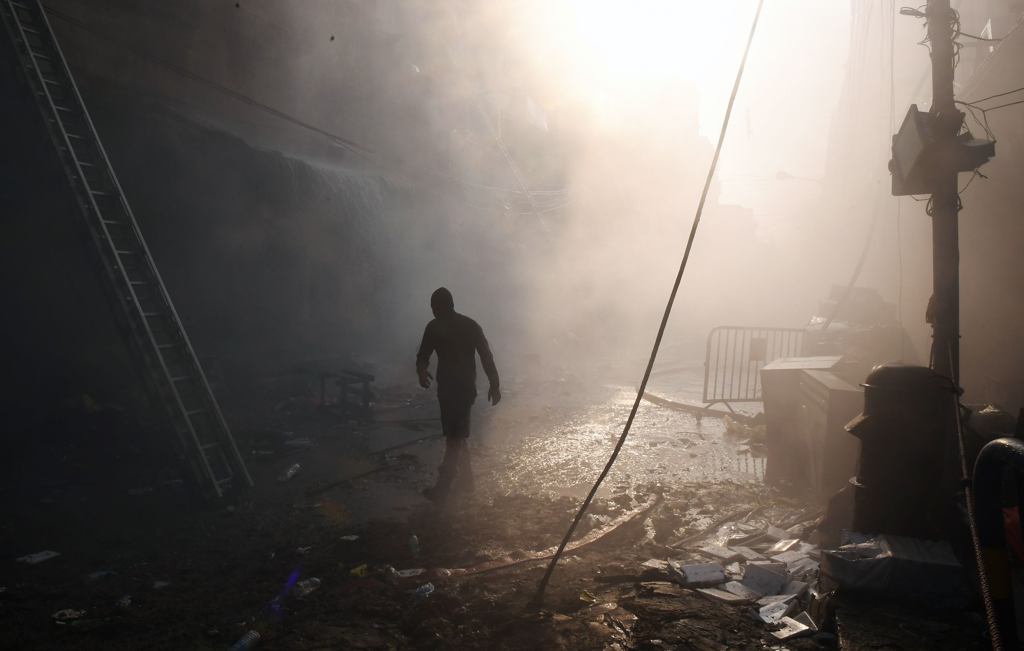 A man walks through mist from Indian firefighters spraying water to extinguish a fire at the Bagree market building in Kolkata.