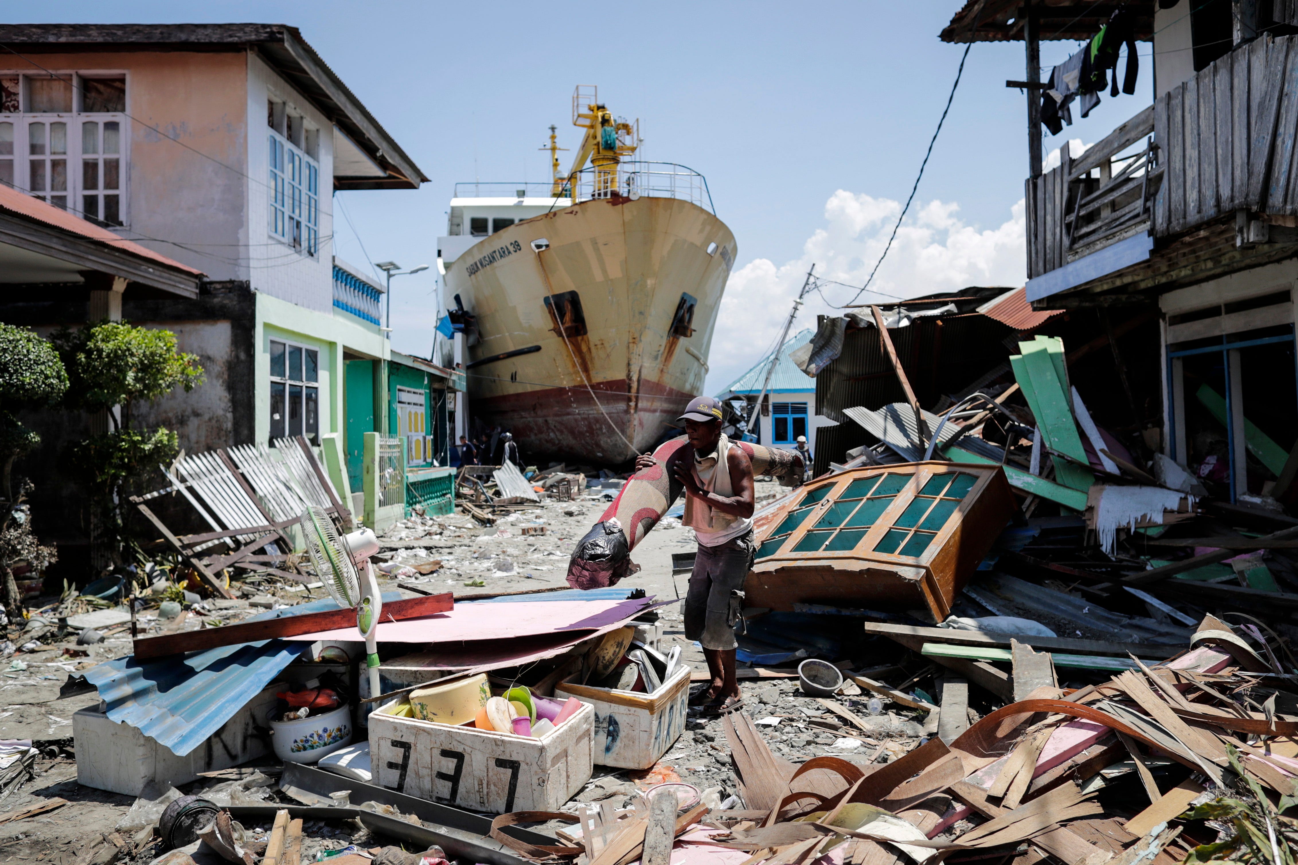 An Indonesian man carries his belongings past a stranded ship at a tsunami devastated area in Wani, Donggala, Central Sulawesi, Indonesia on Oct. 2, 2018. According to reports, at least 1,234 people have died after a series of powerful earthquakes hi