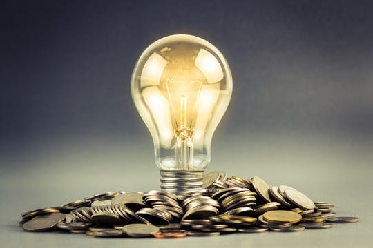 A lit up lightbulb resting on a pile of coins.