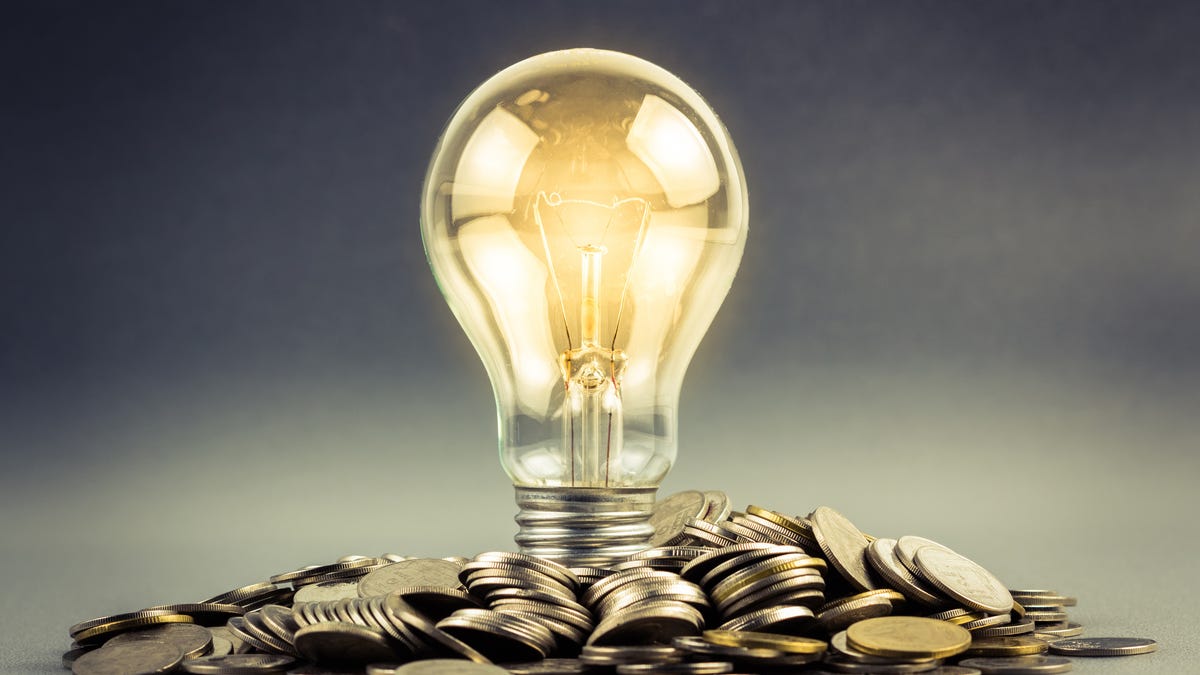 A lit up lightbulb resting on a pile of coins.