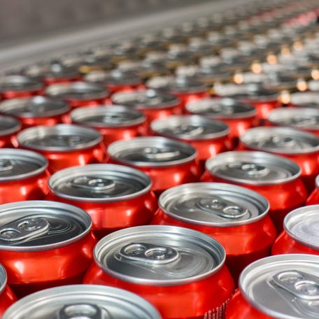 Rows of red aluminum soda cans seen from overhead in a manufacturing facility.
