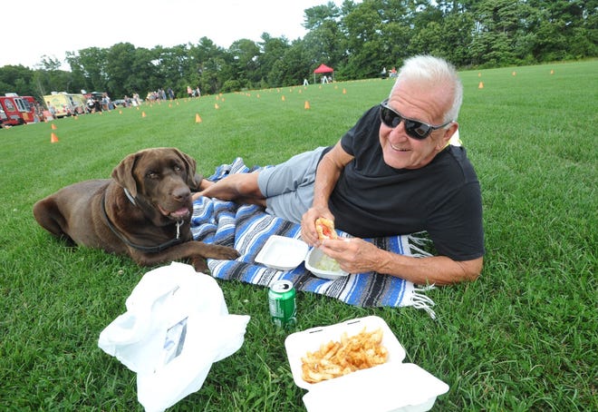 Tony Trigler, of Hanson, relaxes with his dog, Amigo, while enjoying a chicken sandwich at the Food Truck Tuesdays event at Forge Pond Park in Hanover sponsored by the South Shore Food Truck Association, Tuesday, Aug. 25, 2020.