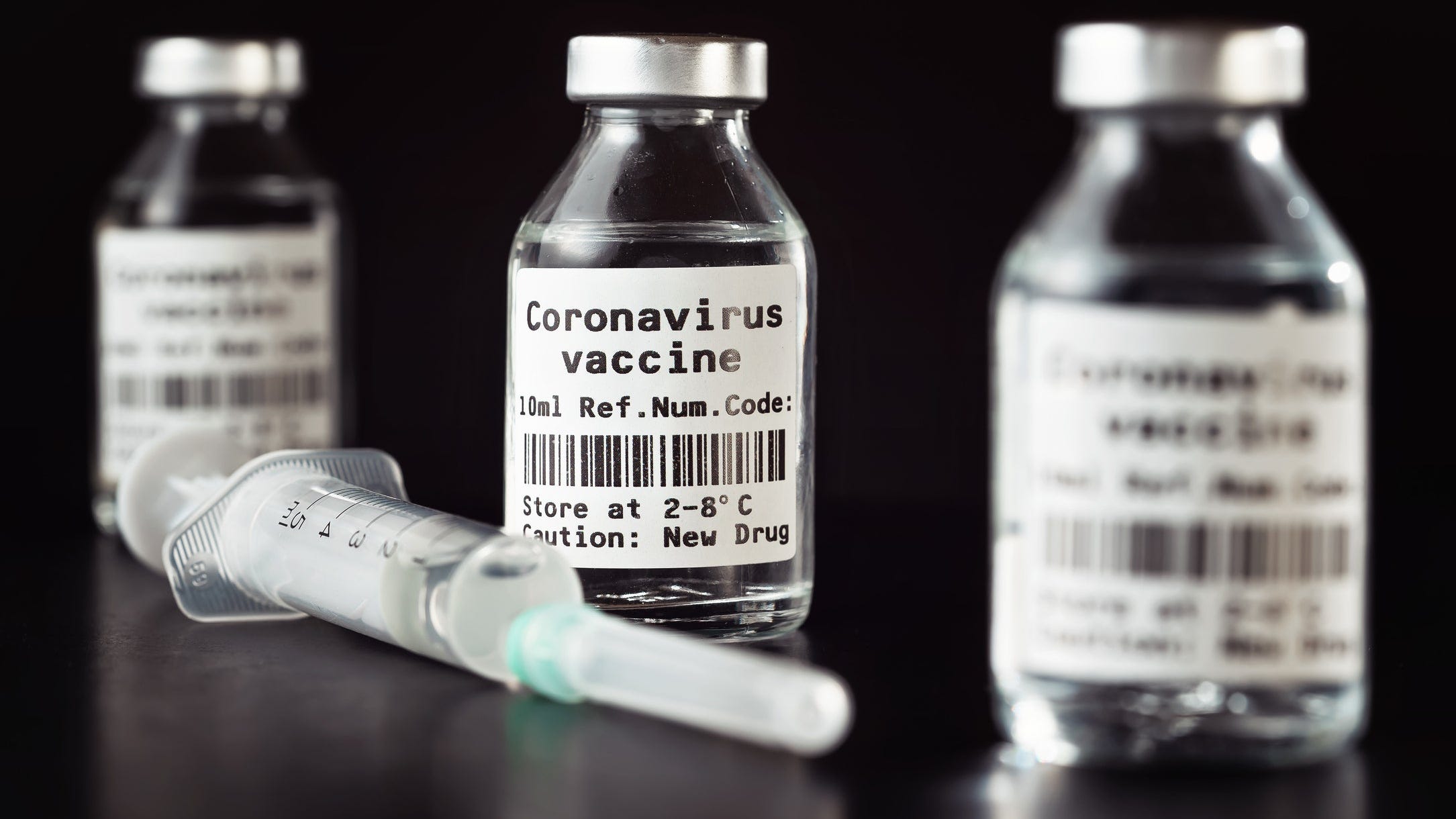 Three vaccine bottles that say Coronavirus vaccine next to a syringe.