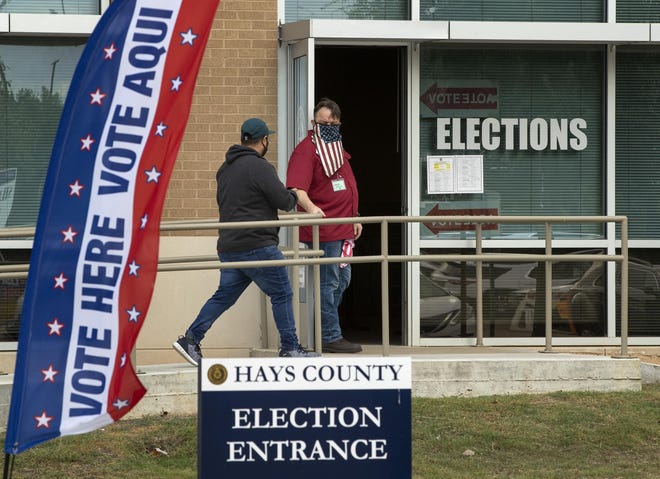Election clerk Wes Garcia, right, holds the door for a voter Monday at an early voting location at the Hays County Elections Office in San Marcos. A federal judge late Tuesday ordered that masks be worn in polling places.
