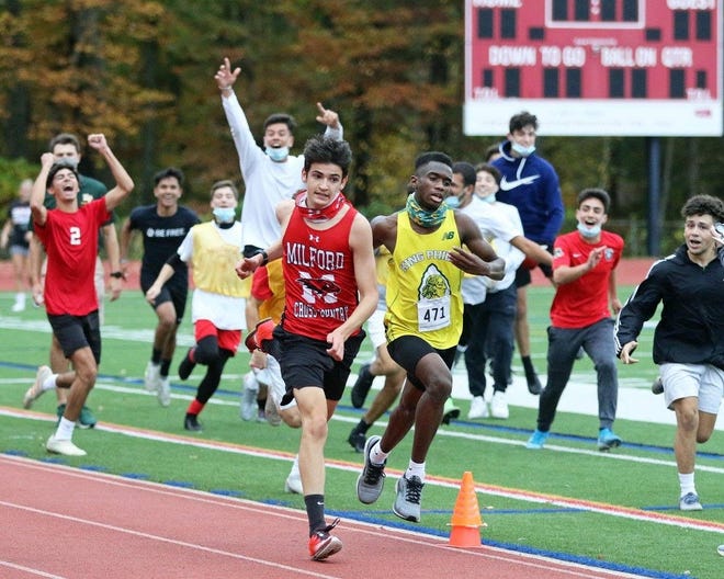 Milford High junior James Comisky (left) races past King Philip's Javon Joseph in a cross country meet on Wednesday at Milford High School. Comisky won the race as the Milford High boys soccer team watched the finish.