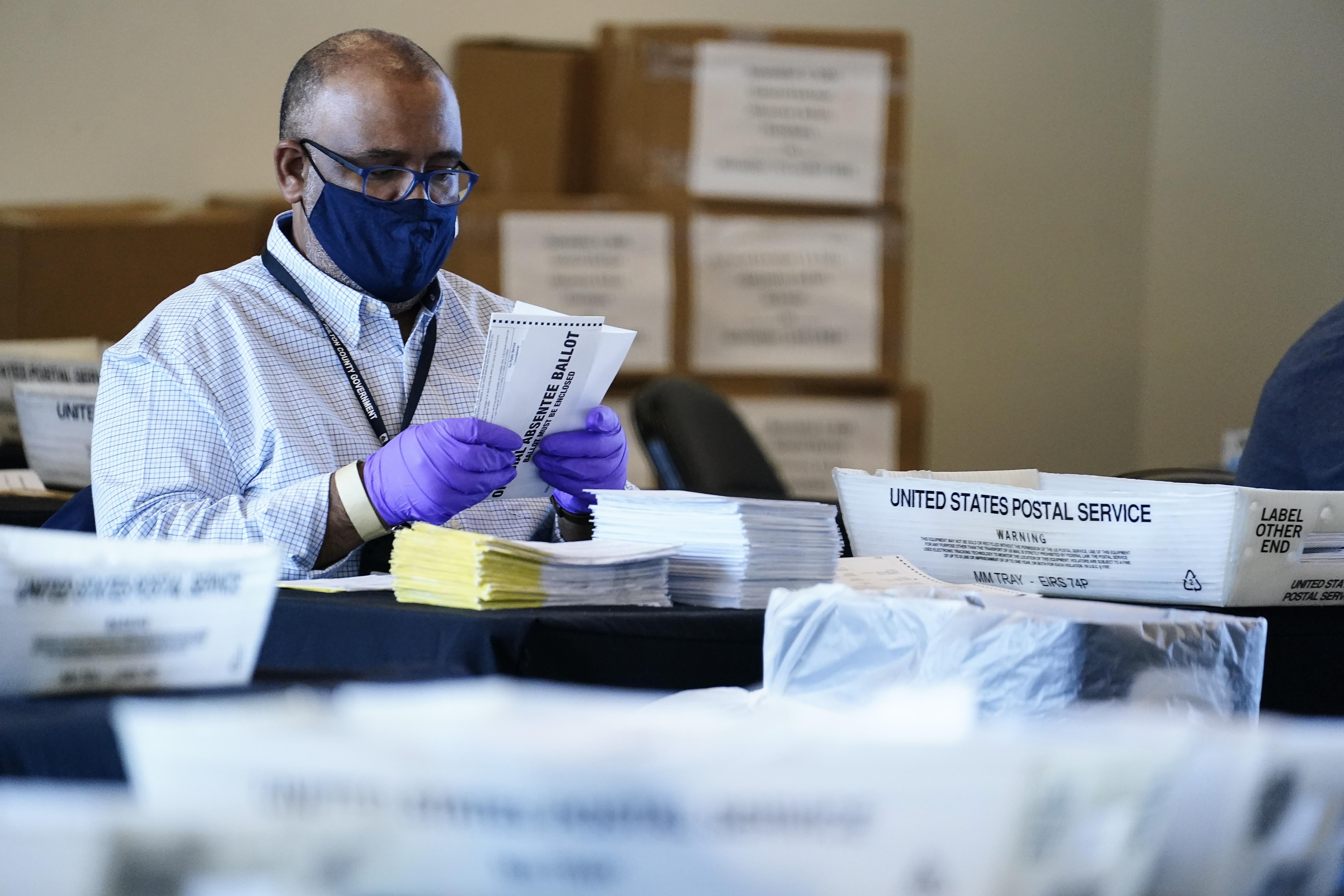 An election inspector looks at an absentee ballot as vote counting in the general election continues at State Farm Arena, Wednesday, Nov. 4, 2020, in Atlanta.