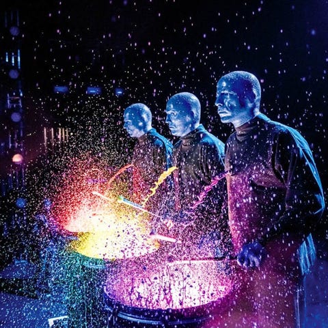 Three Blue Man Group performers playing drums in c