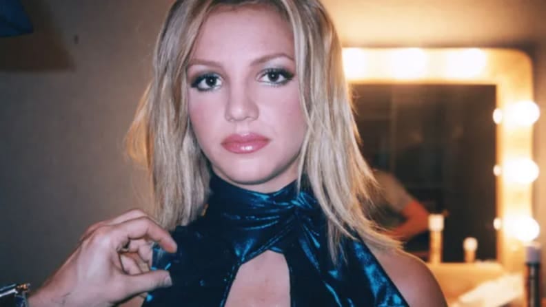 Britney Spears stares at the camera as a hand is seen fixing her top.