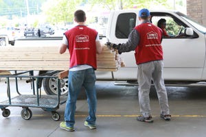 Two Lowe's employees loading some wood into a customer's white pickup truck.