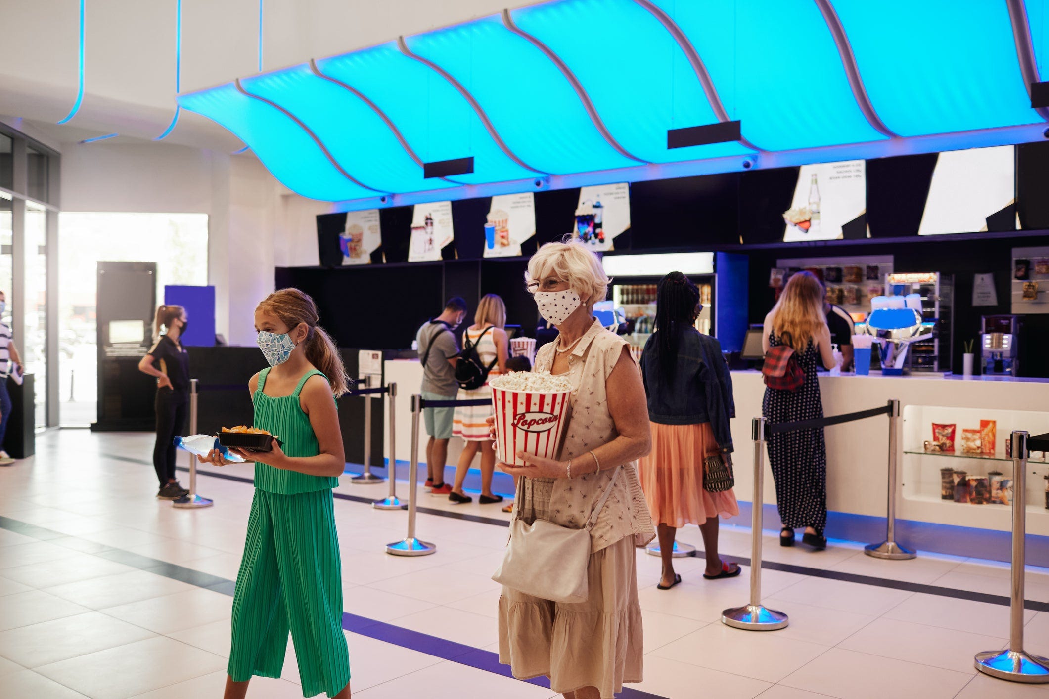 Masked moviegoers leaving a theater concession stand with their purchases