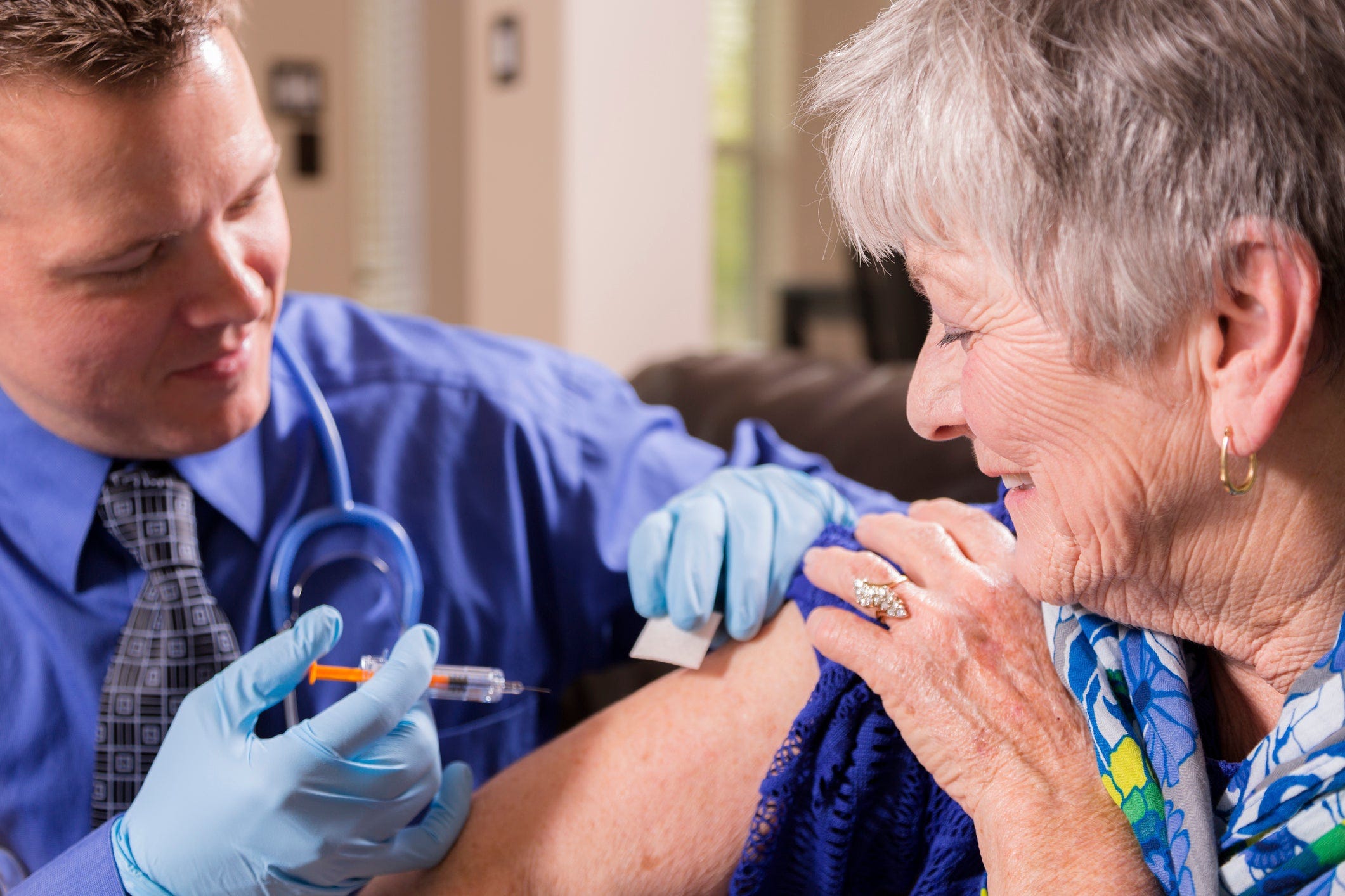 A physician administering a vaccine into the arm of an elderly woman.