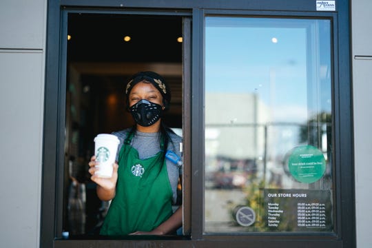 A Starbucks employee hands a cup out through a drive-up window at a Starbucks restaurant.