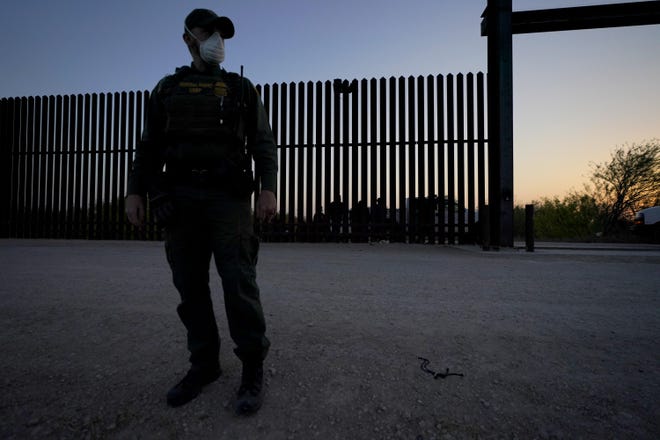 A U.S. Customs and Border Protection agent stands on guard near a gate on the U.S.-Mexico border wall as agents take migrants into custody in Abram-Perezville, Texas.