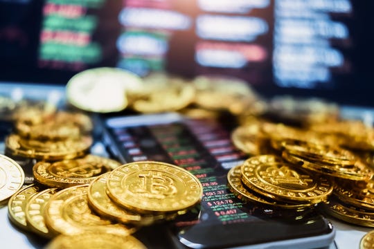 An assortment of physical Bitcoin laid atop a smartphone displaying crypto quotes and charts.