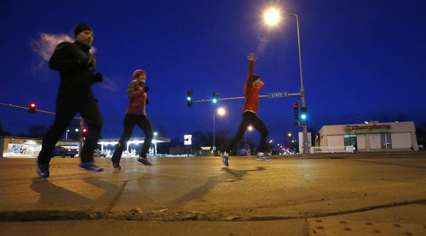 Kevin Bjerke, right, celebrates the completion of a morning run as he and Sonya Nilsson, center and Dave Derzab, left, cross Sixth Avenue Southeast along South State Street Tuesday morning at approximately 6:40 a.m. photo by john davis taken 4/2/2013