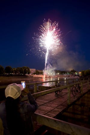 A woman photographs fireworks exploding over the St. Joseph River during Meet Me on the Island on Thursday night in downtown South Bend. (SBT Photo/JAMES BROSHER)