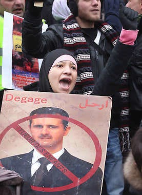 A woman holding a portrait of Syrian President Bashar Assad chants slogans during an anti-regime protest Sunday in Brussels. The text says: “Go away, murderer of children.”Yves Logghe | Associated Press