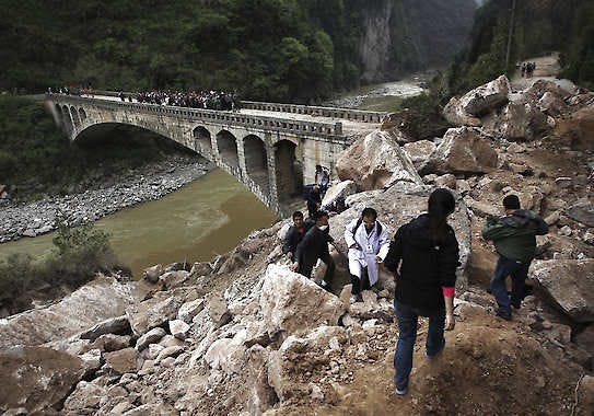 People walk on rocks from a landslide Sunday triggered by a strong earthquake Saturday in southwestern China’s Sichuan province. The quake killed at least 186 people, China’s Xinhua News Agency said. Associated Press