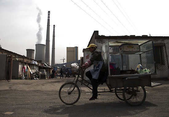 A vendor rides his tricycle Friday near a coal-fired power plant in Beijing. China, the world’s largest producer of carbon dioxide, is directly feeling the man-made heat of global warming, scientists conclude in the first study to link the burning of fossil fuels to one country’s rise in its daily temperature spikes.Andy Wong | Associated Press