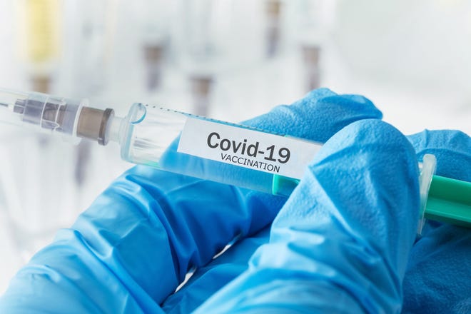 A person wearing safety gloves is holding a COVID-19 vaccine syringe.
