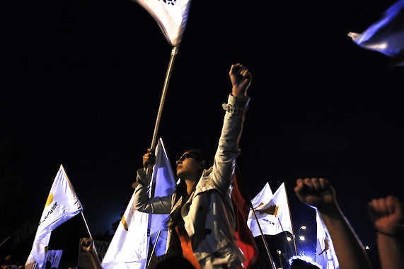 A protester waves a Cyprus flag during a rally Wednesday outside the Cypriot presidential palace in the capital, Nicosia. Cypriot authorities set limits on how much money depositors can take out of their accounts a day before banks were set to reopen. Petros Karadjias | Associated Press
