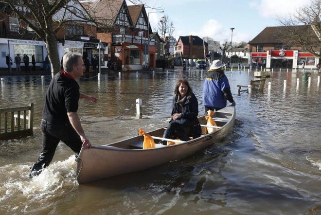 Sang Tan | Associated PressA woman sits in a boat pushed by her companions through a flooded street Monday in Datchet, England.