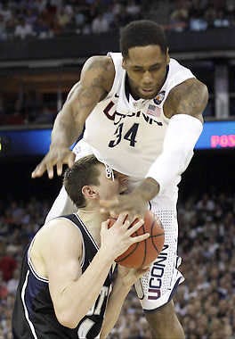 HOUSTON — Connecticut’s Alex Oriakhi topples over Butler’s Andrew Smith during the first half of the NCAA championship game Monday night. (Associated Press).