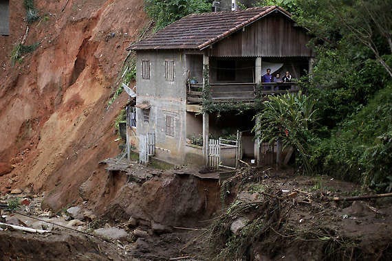 People stand on the porch of their home at the edge of landslide damage Thursday in the Caleme neighborhood in Teresopolis, Brazil.Felipe Dana | Associated Press
