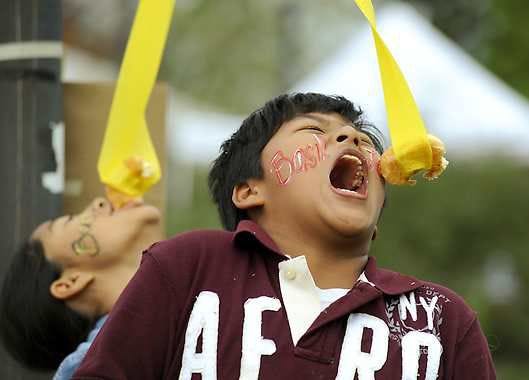 Nelson Mai, front, and Khathy Thach participate in the doughnut dangle, in which visitors try to eat a doughnut hanging from a ribbon, Saturday at the Pumpkin Party at Hilltop Gardens and Nature Center. (Herald-Times / MONTY HOWELL)