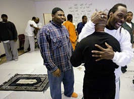 Muslim inmates Mark Anthony Aikens, in white, hugs fellow Muslim inmate Ricardo Searles after weekly Friday worship March 11 in a room used as a makeshift mosque at Rikers Island prison, on New York\'s East River. Stephan Savoia | Associated Press