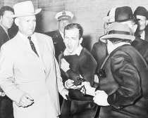 Lee Harvey Oswald, accused assassin of President John F. Kennedy, reacts as Dallas night club owner Jack Ruby, foreground, shoots at him from point-blank range in a corridor of Dallas police headquarters, in this Nov. 24, 1963 file photo. The plainclothesman at left is Jim A. Leavelle. AP Photo.
