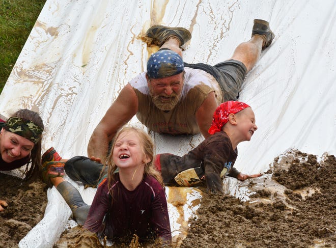 Participants splash into the mud at the bottom of the slip and slide obstacle Saturday in the Windber 5K Obstacle Challenge.