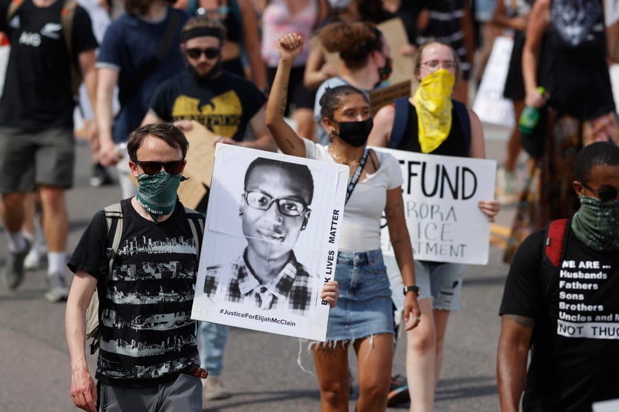 Demonstrators carry placards during a June 27, 2020, rally and march over the death of Elijah McClain in Aurora, Colo.