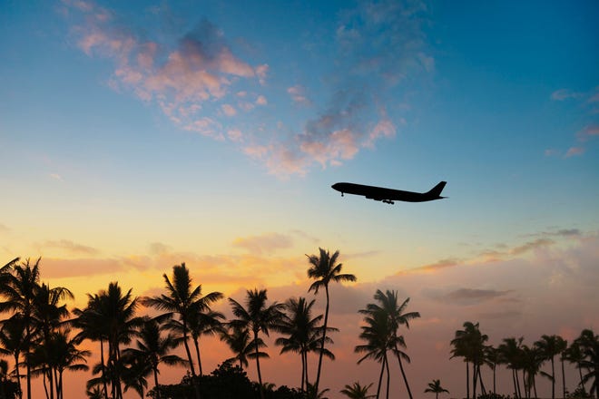 A plane flies over a tropical scene.
