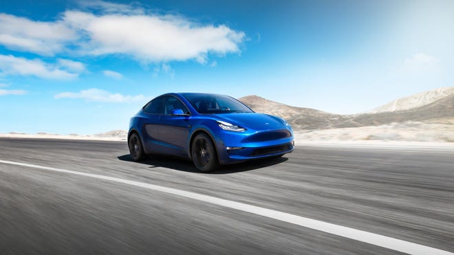 A blue Tesla electric vehicle driving fast on the open road.