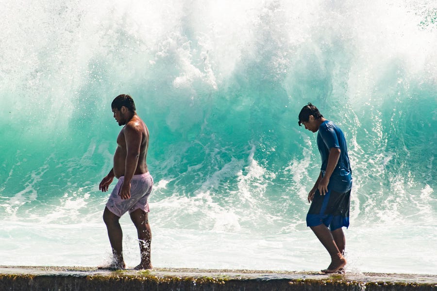 People walk in front of the high surf near Kapahulu Groin (Waikiki Wall) in Waikiki, Hawaii, on Sunday.
