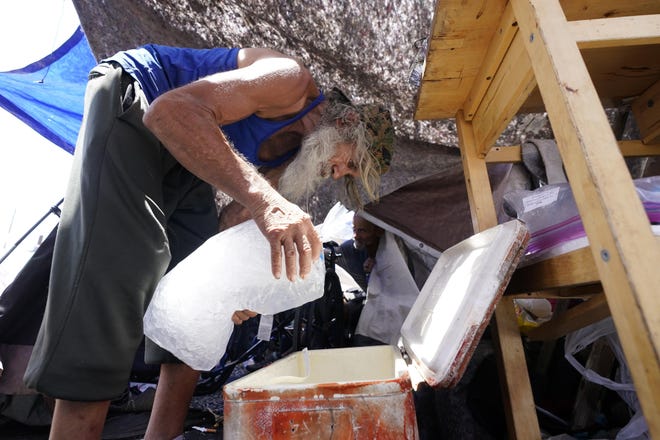 Roberto Delaney places a bag of ice inside a cooler as he tries to stay cool inside his tent at a homeless encampment in Phoenix.