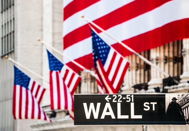 An American flag draped over the New York Stock Exchange, with the Wall St. street sign in the foreground.