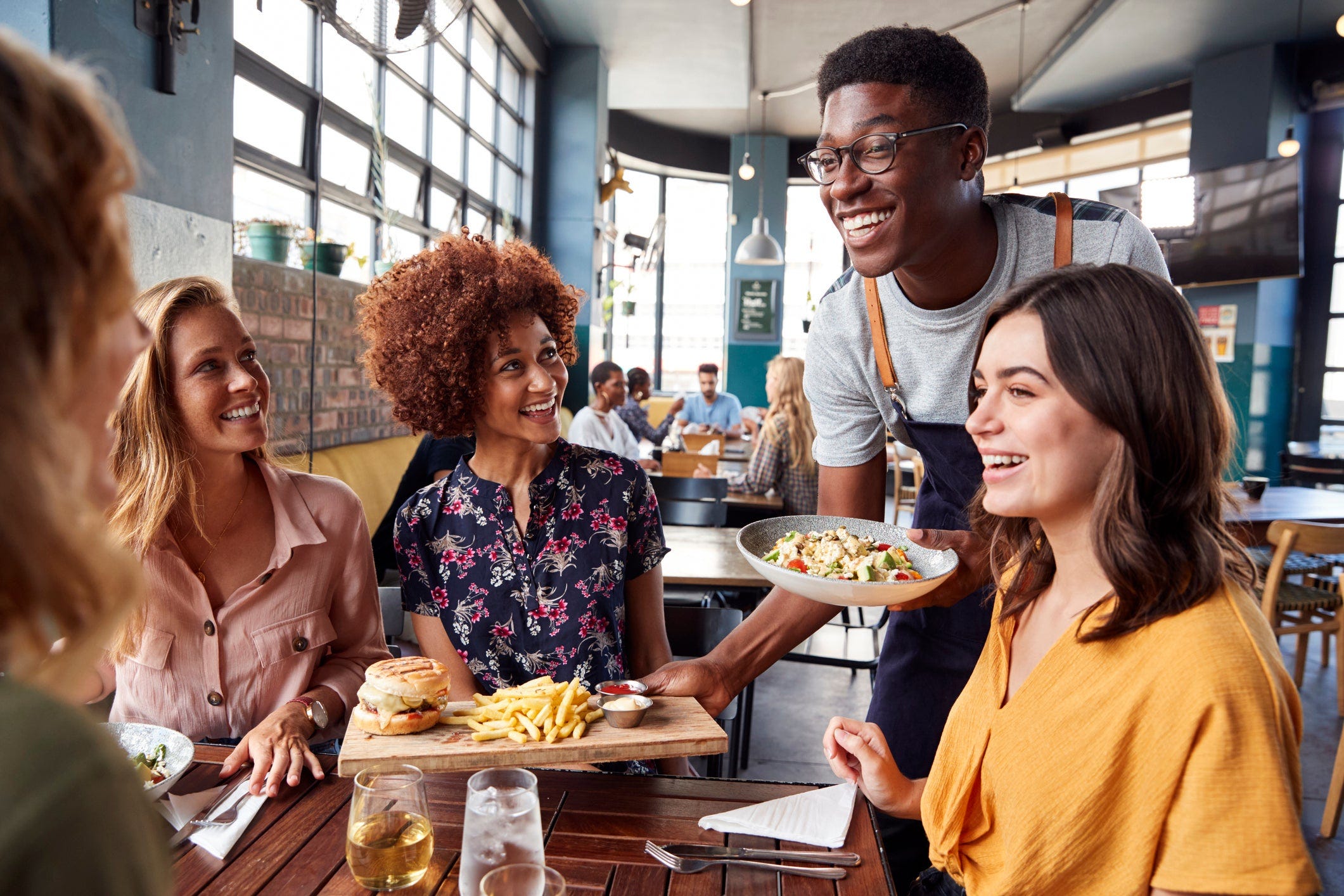 A server bring food to a table of restaurant patrons.
