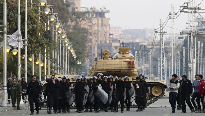 Egyptian riot police walk past a military tank guarding the presidential palace in Cairo Sunday.