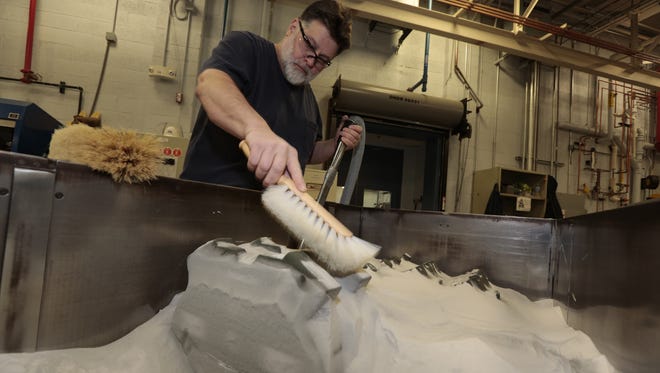 Dennis DuBay at Ford removes sand  that surrounds parts for a block core package (sand cast mold for engine components)  that was made with a 3-D printing process at a Ford facility in Dearborn Heights, Mich.