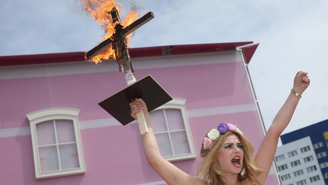 A bare-breasted protester with an inscription on her body that reads "Life In Plastic Is Not Fantastic" yells protest slogans while holding up a burning cross with a Barbie doll attached to it outside the Barbie Dreamhouse Experience on Thursday in Berlin, Germany.