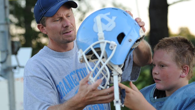 Kevin Guskiewicz, a UNC professor and researcher who has been studying concussions, helps his son Adam with is helmet at a Pop Warner League football practice in 2011.