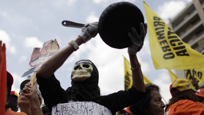 A protester dressed as a death holds up pan during an opposition demonstration against of the devaluation of the currency in Caracas, Venezuela, Saturday, Feb. 23, 2013.