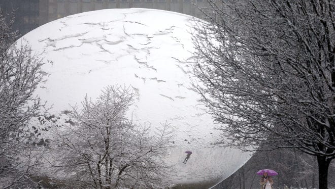 Fresh snow covers Anish Kapoor's sculpture "Cloud Gate" and gives it the appearance of a cracked egg as a lone pedestrian walks around the stainless steel  attraction in Chicago's Millennium Park, as a winter storm of rain and snow begins Tuesday, Feb. 26, 2013.