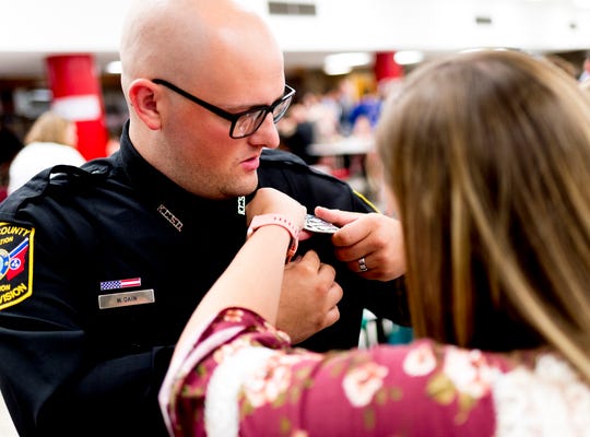 Officer Michael Cain gets help with attaching his badge during a graduation ceremony for school security officers at South-Doyle Middle School in Knoxville, Tennessee on Thursday, July 26, 2018. Knox County Schools graduated twenty-four new officers for the upcoming school year.