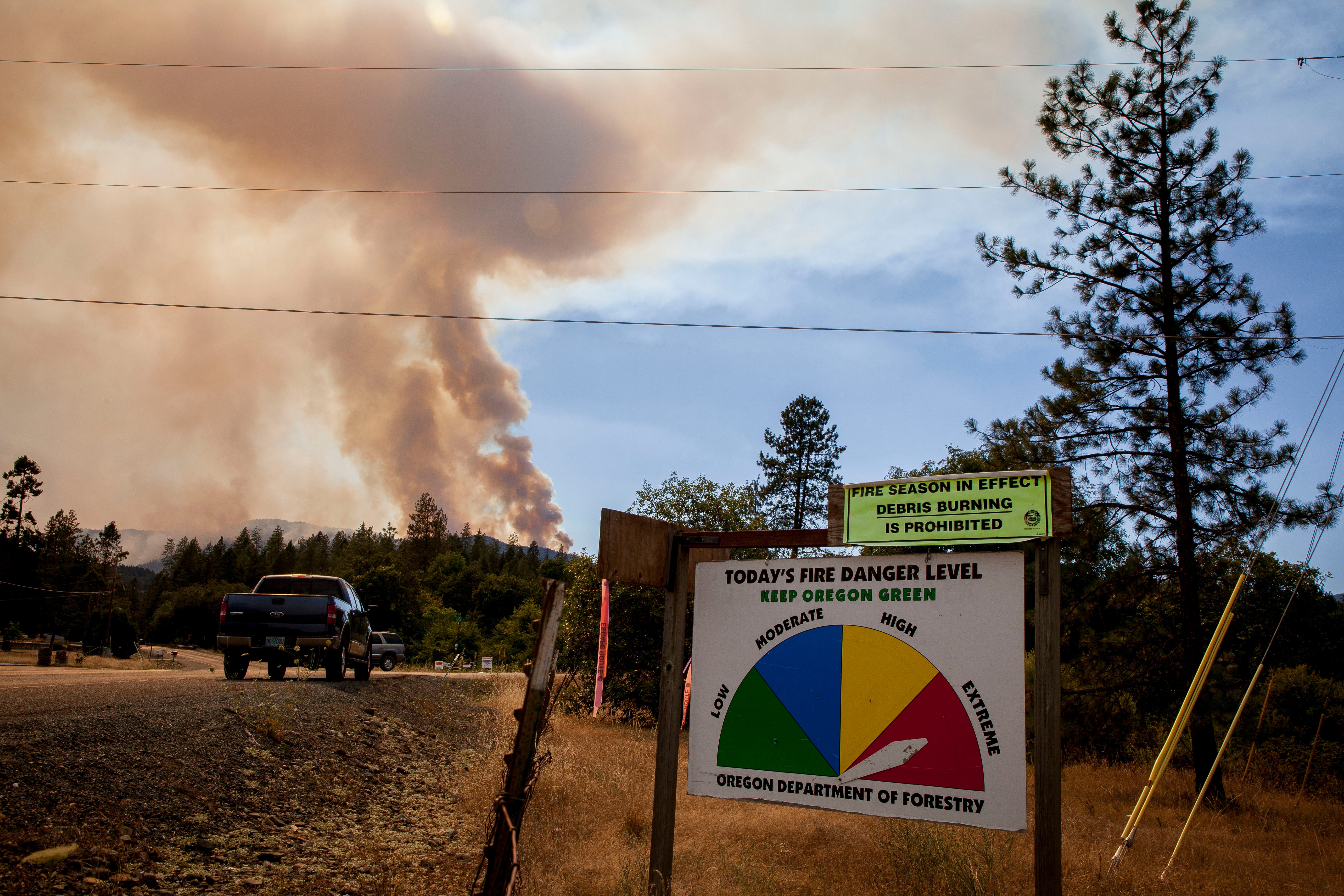 A fire level danger sign shows extreme fire danger along Galice Road just west of Merlin in southern Oregon as smoke rises from Taylor Creek wildfire in the Siskiyou National Forest near the Rogue River in July, 2018.  Smoke caused air quality to be compromised.