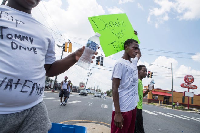 Avery Brown, brother of 12-year-old Ty'mire Selby holds a sign while selling water to help pay for his brother's funeral costs Sunday on Northeast Boulevard. Selby died after a gun went off inside his home on E. 27th Street Friday morning. Police believe the 12-year-old accidentally shot himself, but the investigating isn't over.