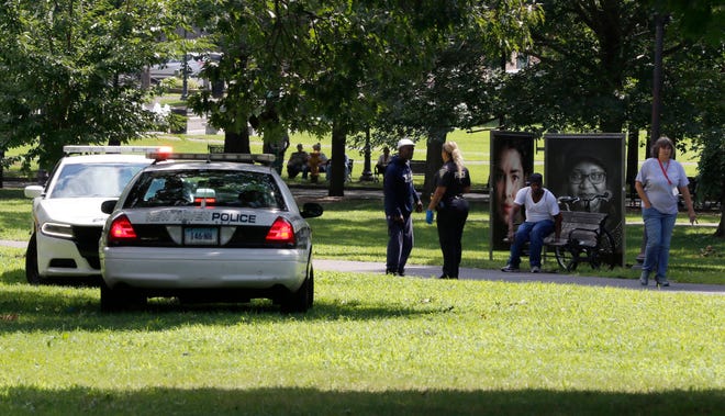 A police officer speaks to a man walking on New Haven Green, Wednesday, Aug. 15, 2018, in New Haven, Conn. A city official said more than a dozen people fell ill from suspected drug overdoses on the green and were taken to local hospitals.